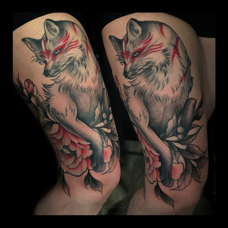 Japanese-inspired thigh tattoo of a mystical kitsune fox with red markings, surrounded by peony flowers and soft black shading